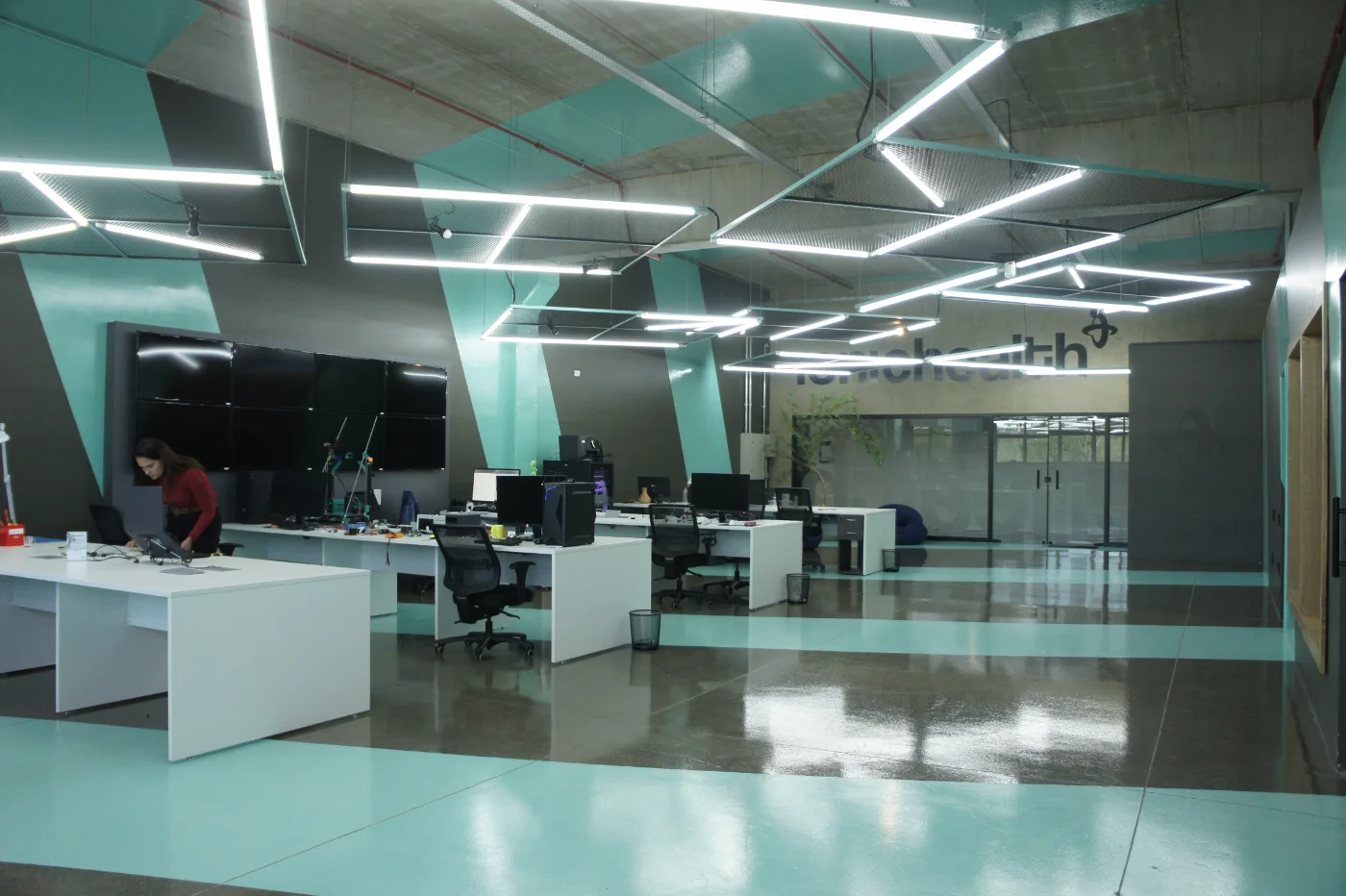 Ionic Health CIT-R: open space com estações de trabalho e grafismo verde-água no piso e paredes