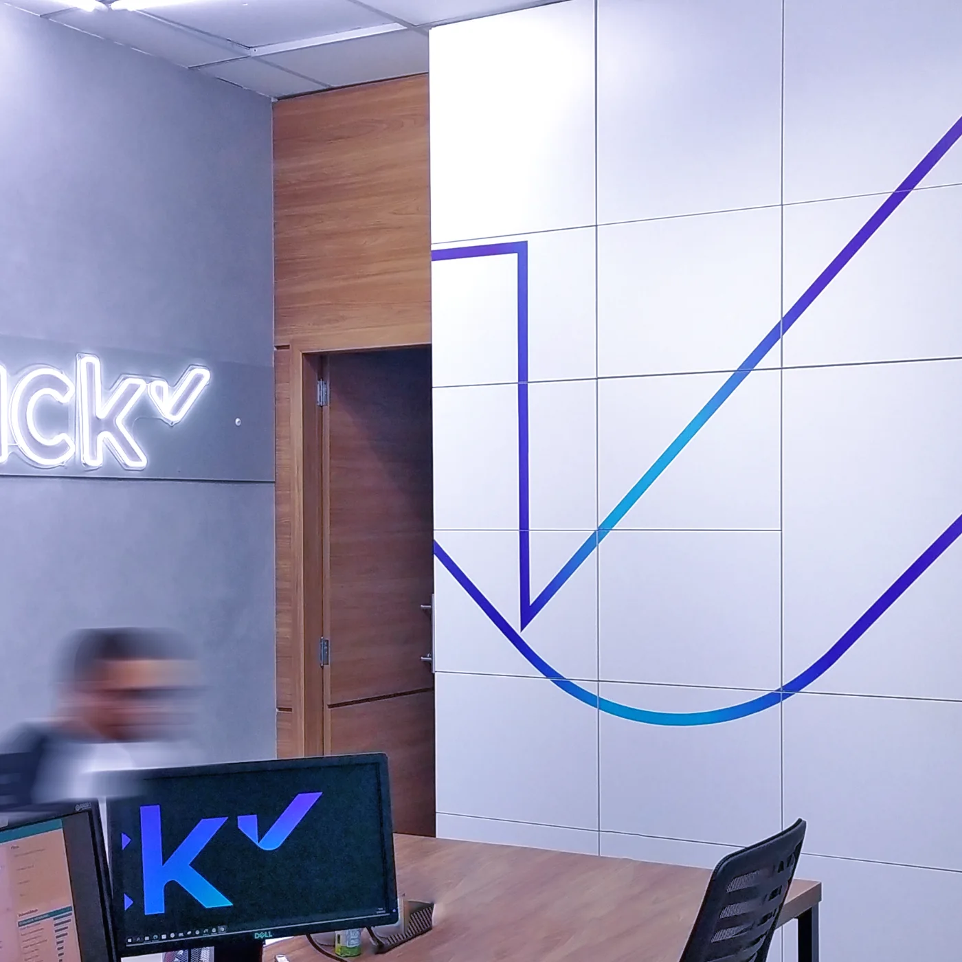 Nick Saúde: recepção com letreiro luminoso da marca sobre painel cinza e grafismo azul na parede modulada