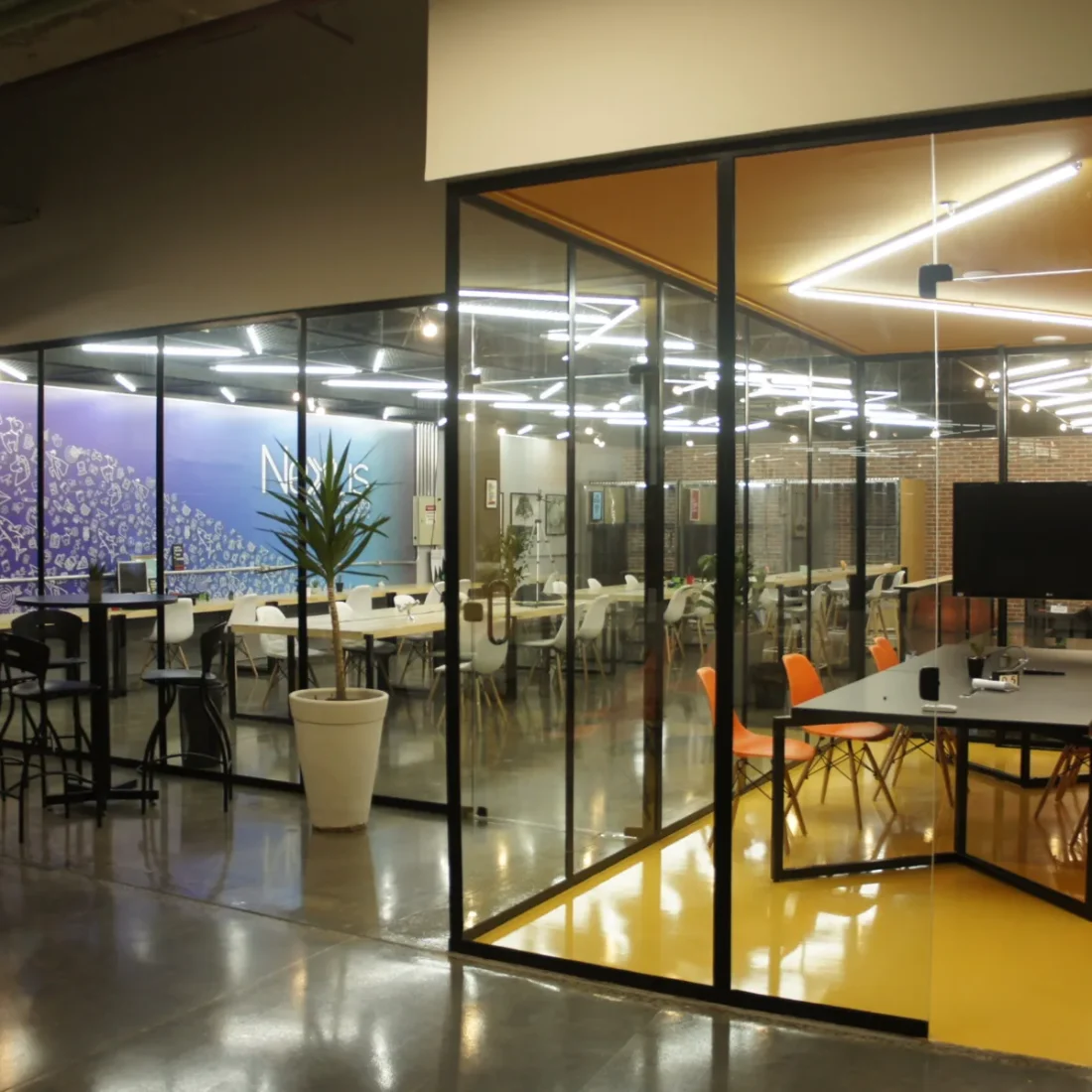 Coworking Netuno: salão com bancadas compartilhadas e sala de reunião de piso amarelo
