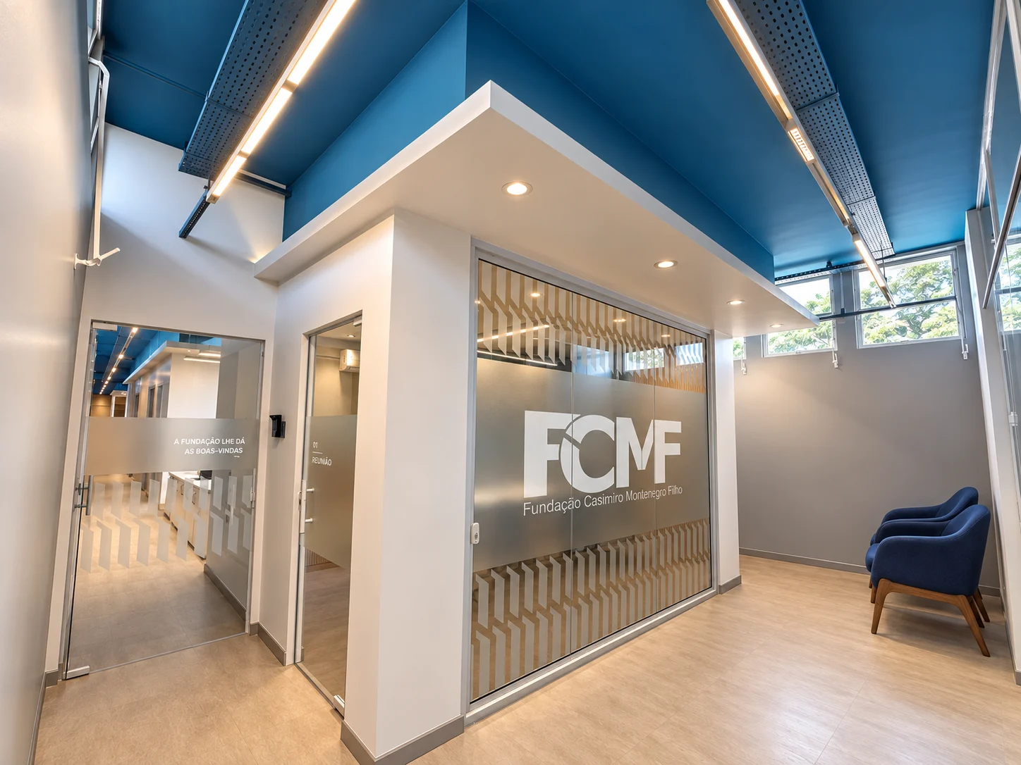 Circulação de acesso ao lobby: divisórias de vidro com a marca da FCMF e grafismo aplicado, sala de reunião 01 à esquerda
