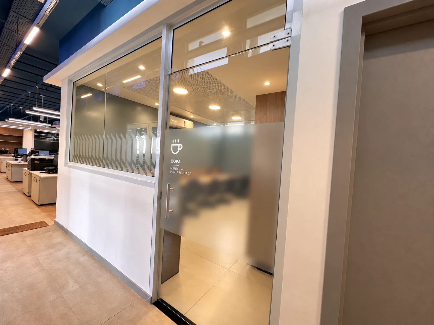 Acesso à copa a partir do open space: caixilho envidraçado com pictograma e orientação de uso aplicados na porta