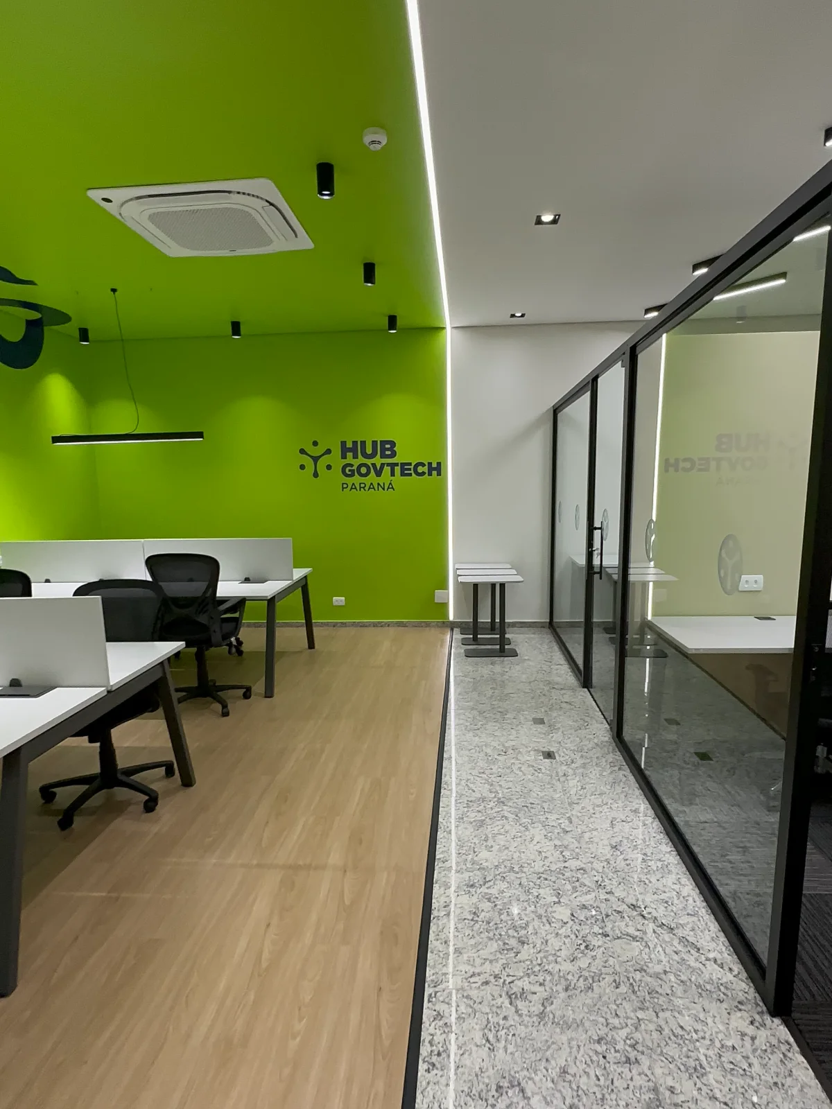 Forro e parede verdes sobre as estações de trabalho, com a marca aplicada e a circulação em granito ao lado das salas envidraçadas