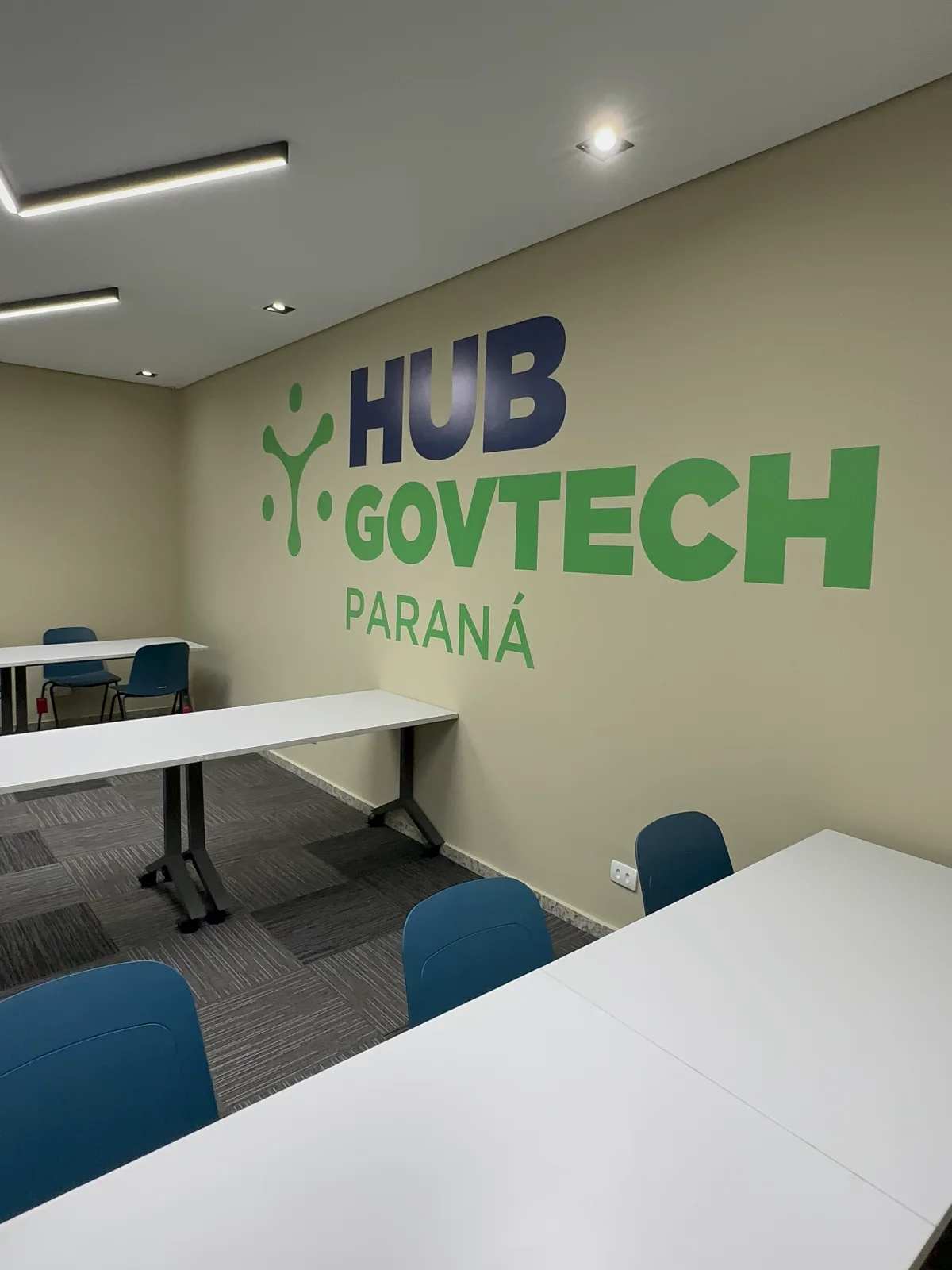 Marca Hub GovTech Paraná aplicada em grande escala na parede da sala de treinamento, em azul e verde