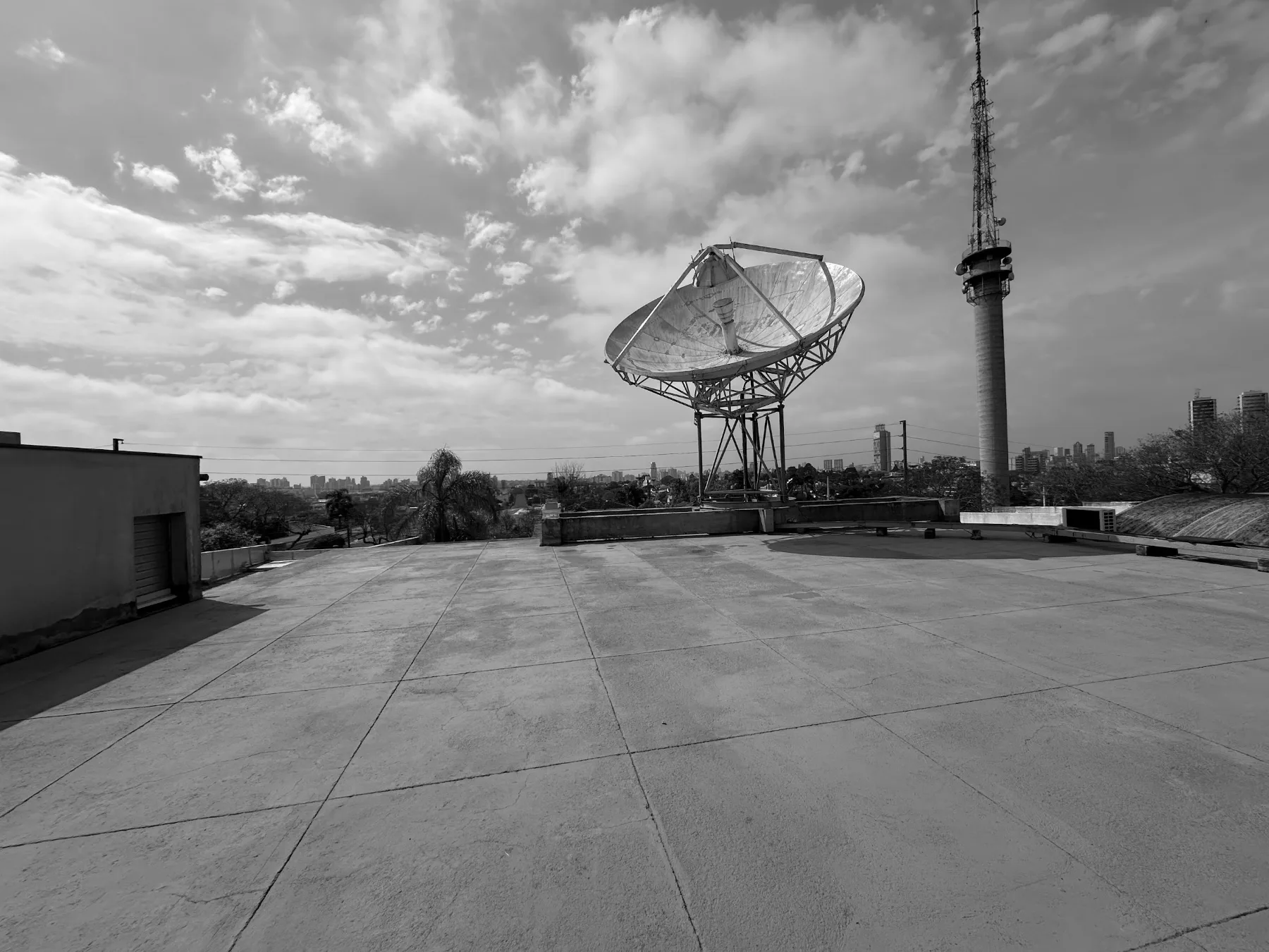 Terraço antes da obra: laje impermeabilizada em placas cinza, antena parabólica de grande porte e torre de transmissão, com a cidade ao fundo