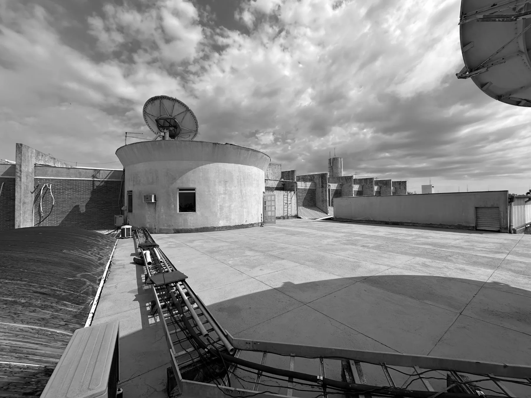 Terraço antes da obra visto em direção ao volume cilíndrico, com eletrocalhas e equipamentos de ar-condicionado sobre a laje
