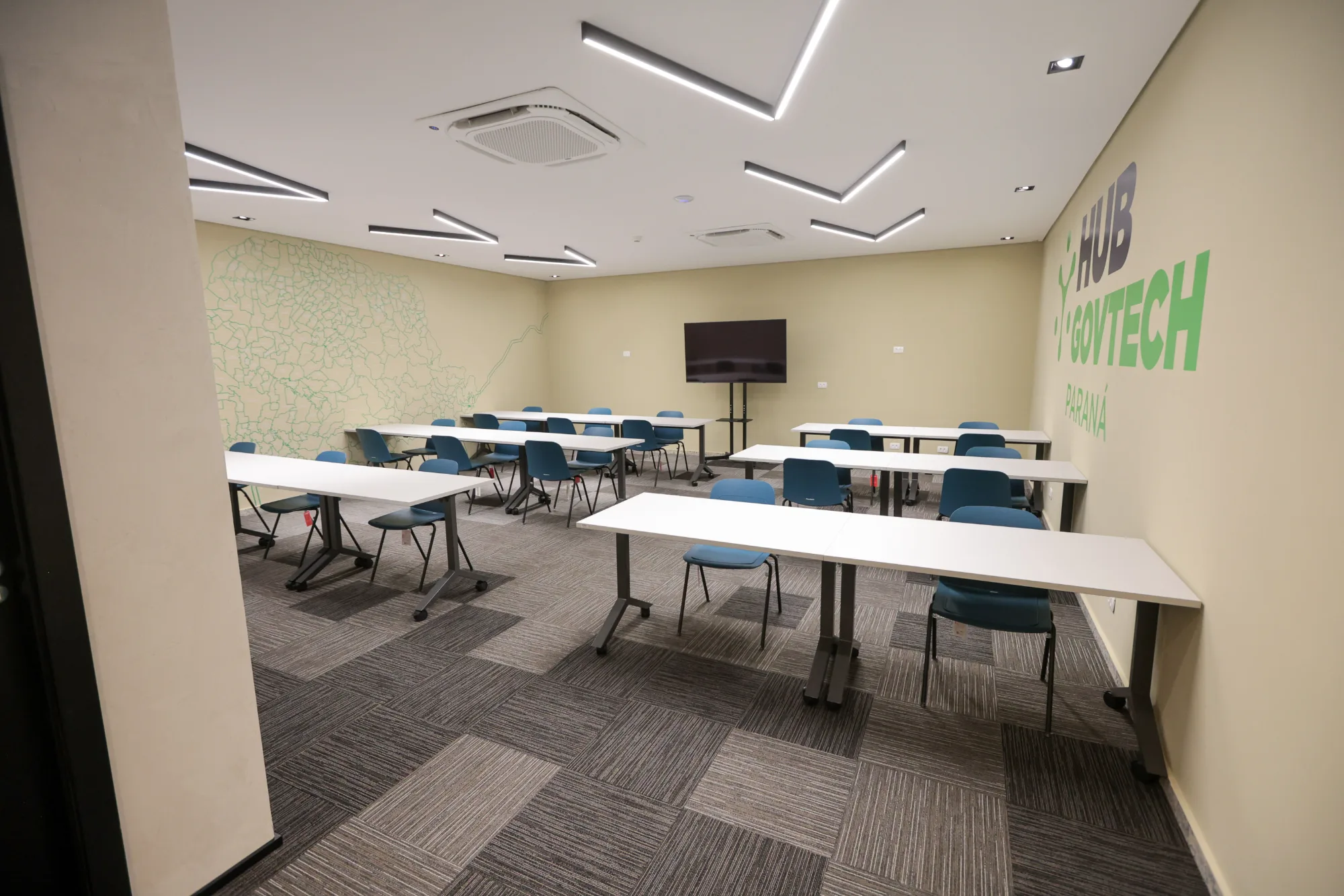 Sala de treinamento em plano geral, com as mesas móveis distribuídas entre o mapa do Paraná e a marca do hub nas paredes