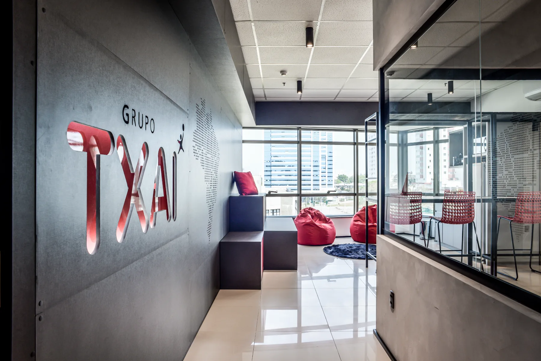 Circulação de chegada do Grupo Txai: marca em relevo sobre painel de concreto, banco corrido e área de convivência junto à fachada envidraçada