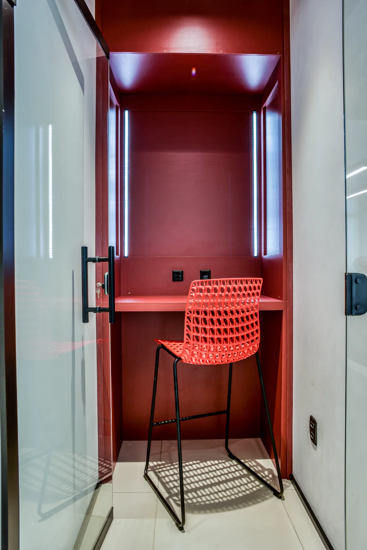 Cabine de foco revestida em vermelho, com bancada, iluminação vertical embutida e fechamento em vidro