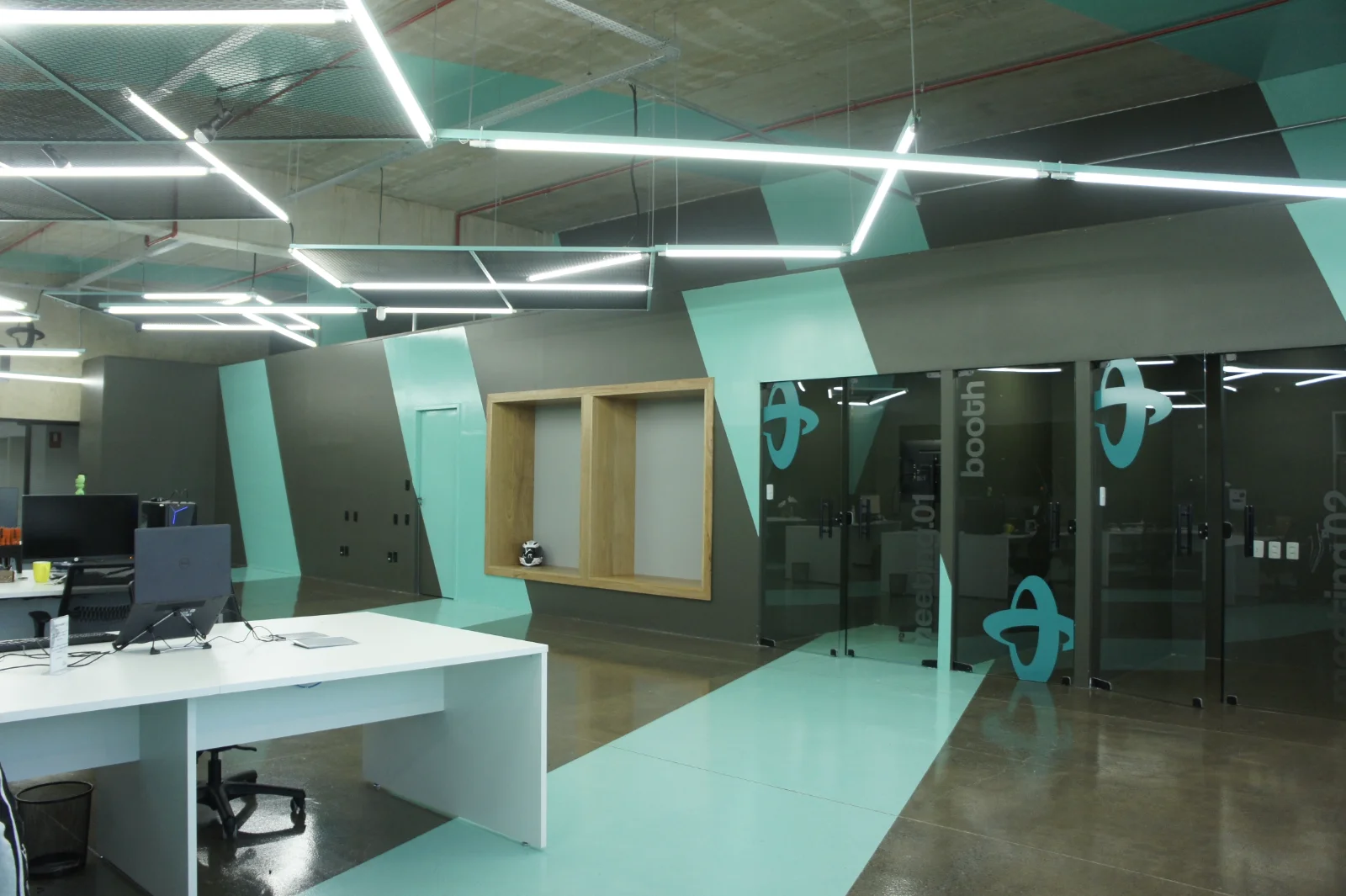 Phone booths envidraçados com aplicação gráfica da marca e sala de reunião ao fundo