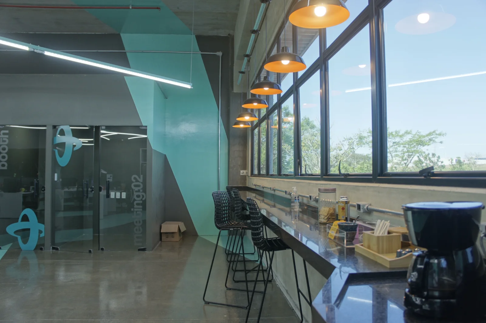 Bancada de convivência junto à fachada envidraçada, com banquetas altas e luminárias pendentes laranja