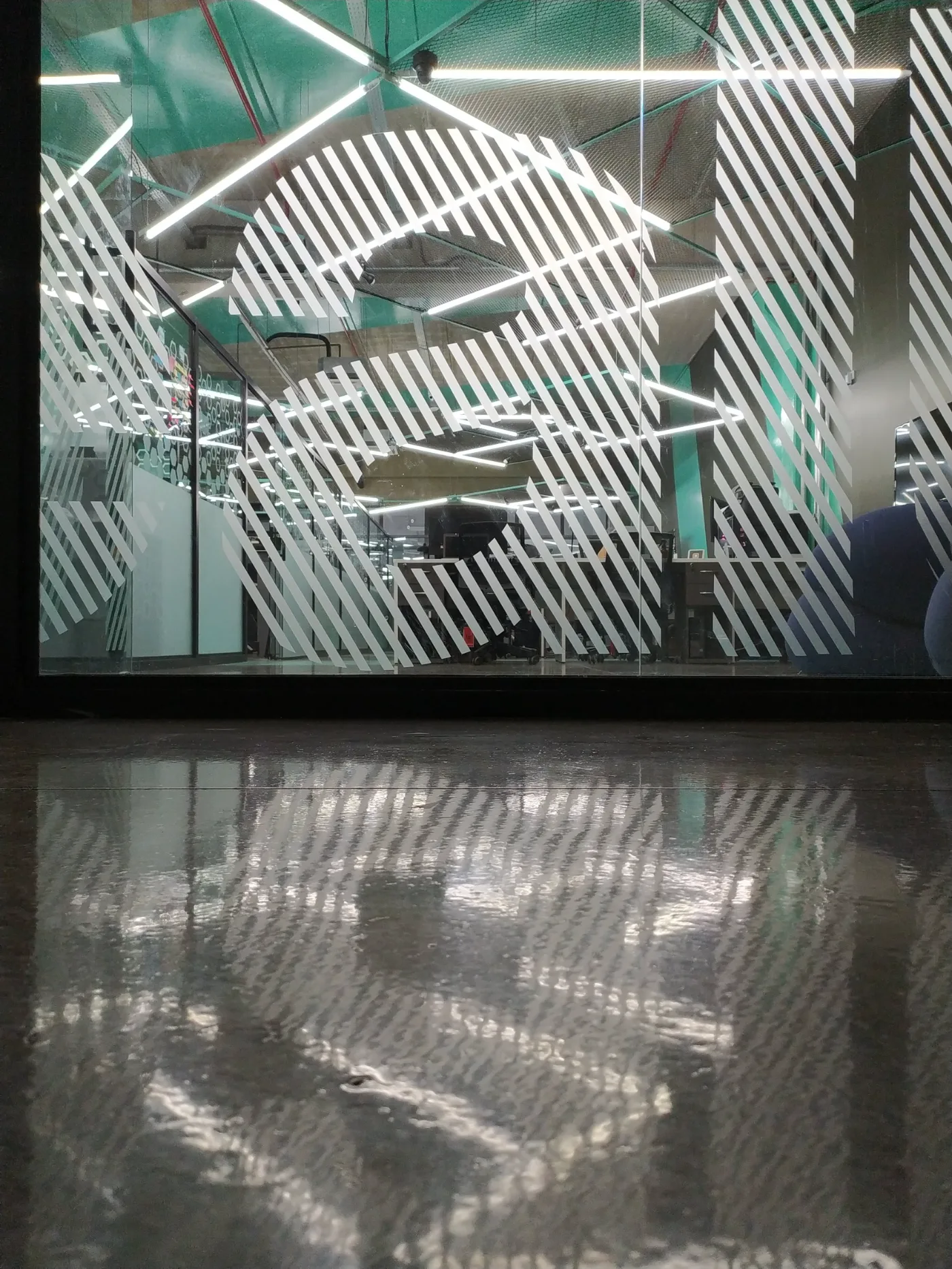 Grafismo diagonal aplicado no vidro da fachada interna, com a iluminação linear refletida no piso