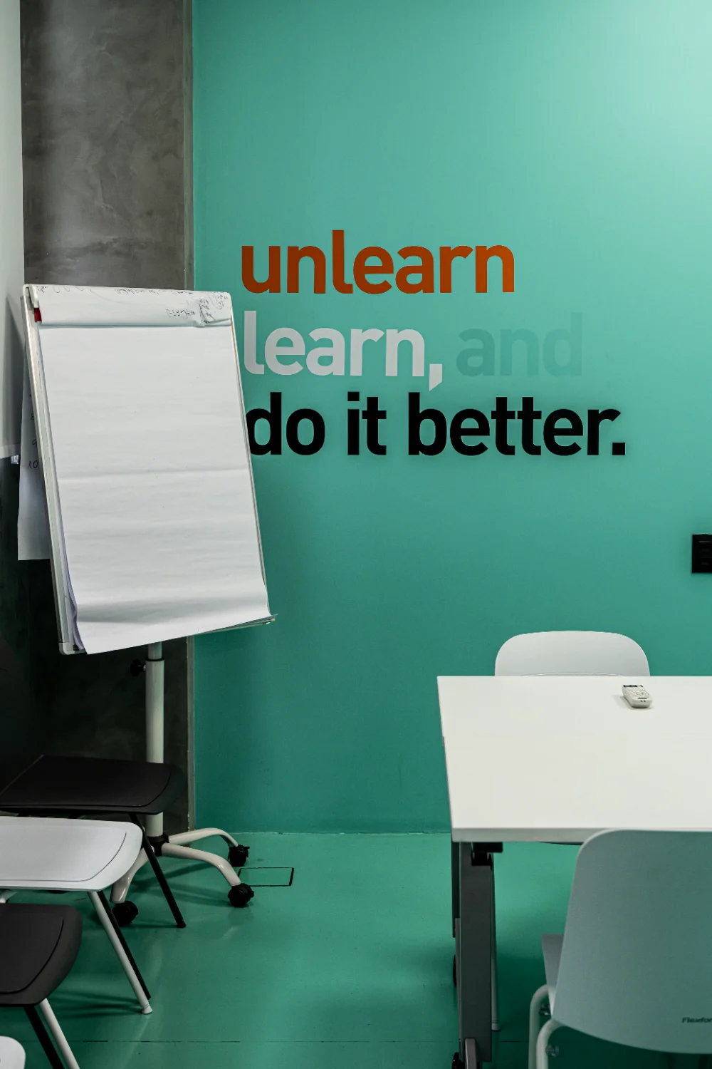 Detalhe da parede verde-água com a frase unlearn, learn, and do it better aplicada em tipografia