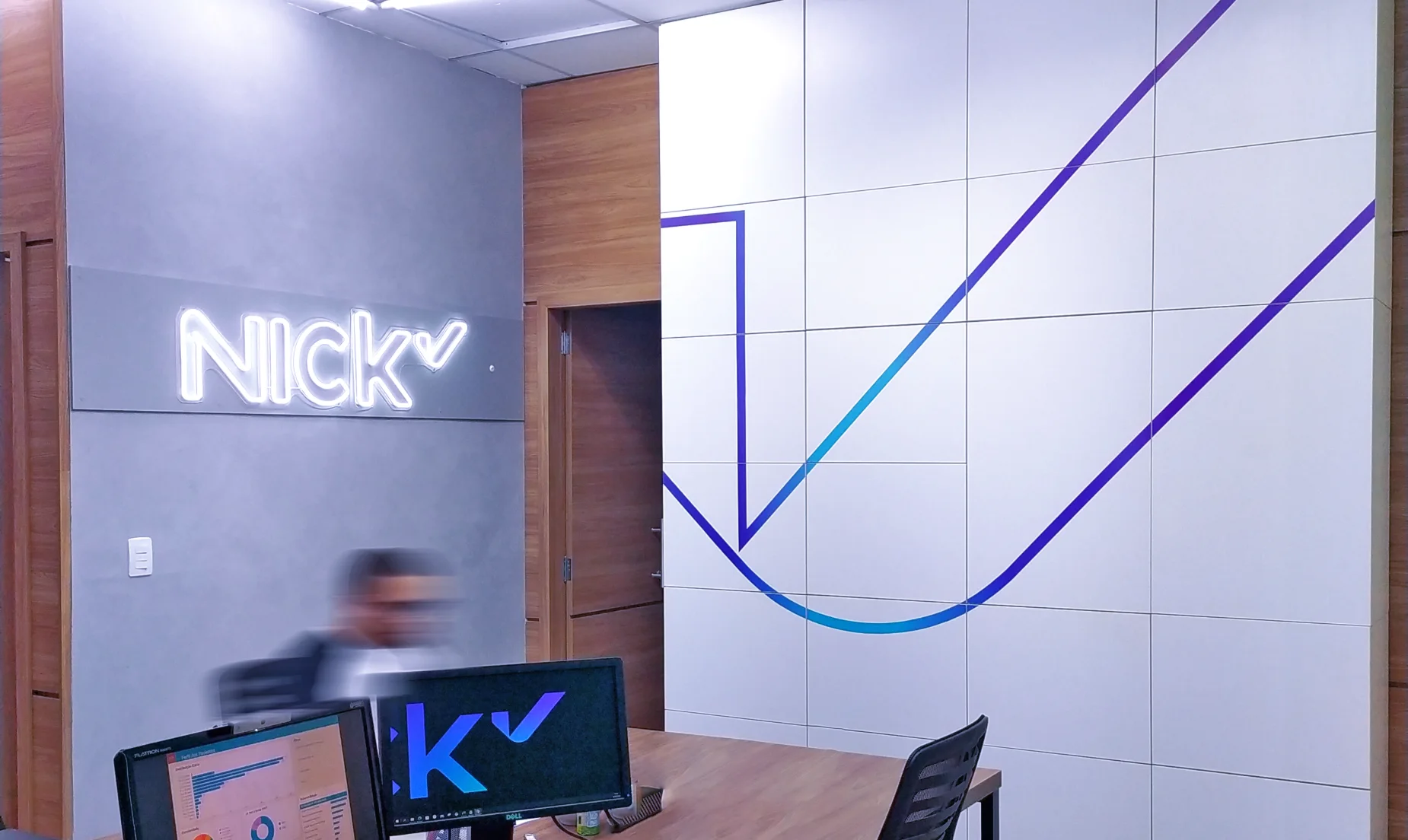 Recepção da Nick Saúde: letreiro luminoso da marca sobre painel cinza e grafismo azul aplicado na parede modulada