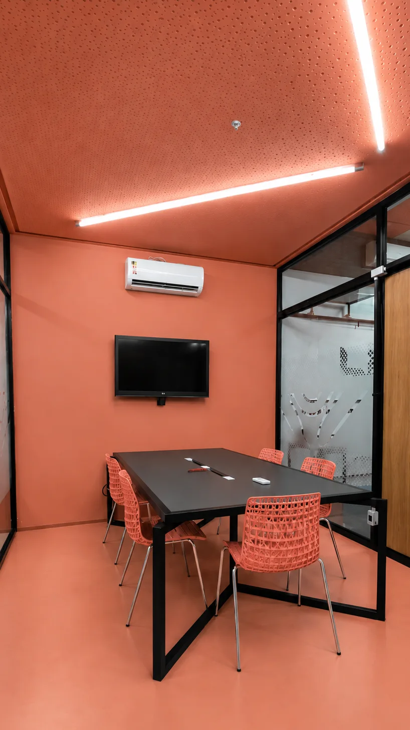 Sala de reunião em coral, com forro acústico perfurado, piso e paredes na mesma cor, mesa preta e cadeiras vazadas coral