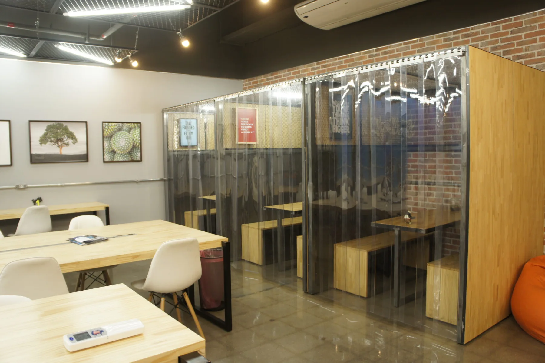 Cabines de conversa com bancos de madeira, fechadas por cortinas de PVC transparente, junto à parede de tijolo