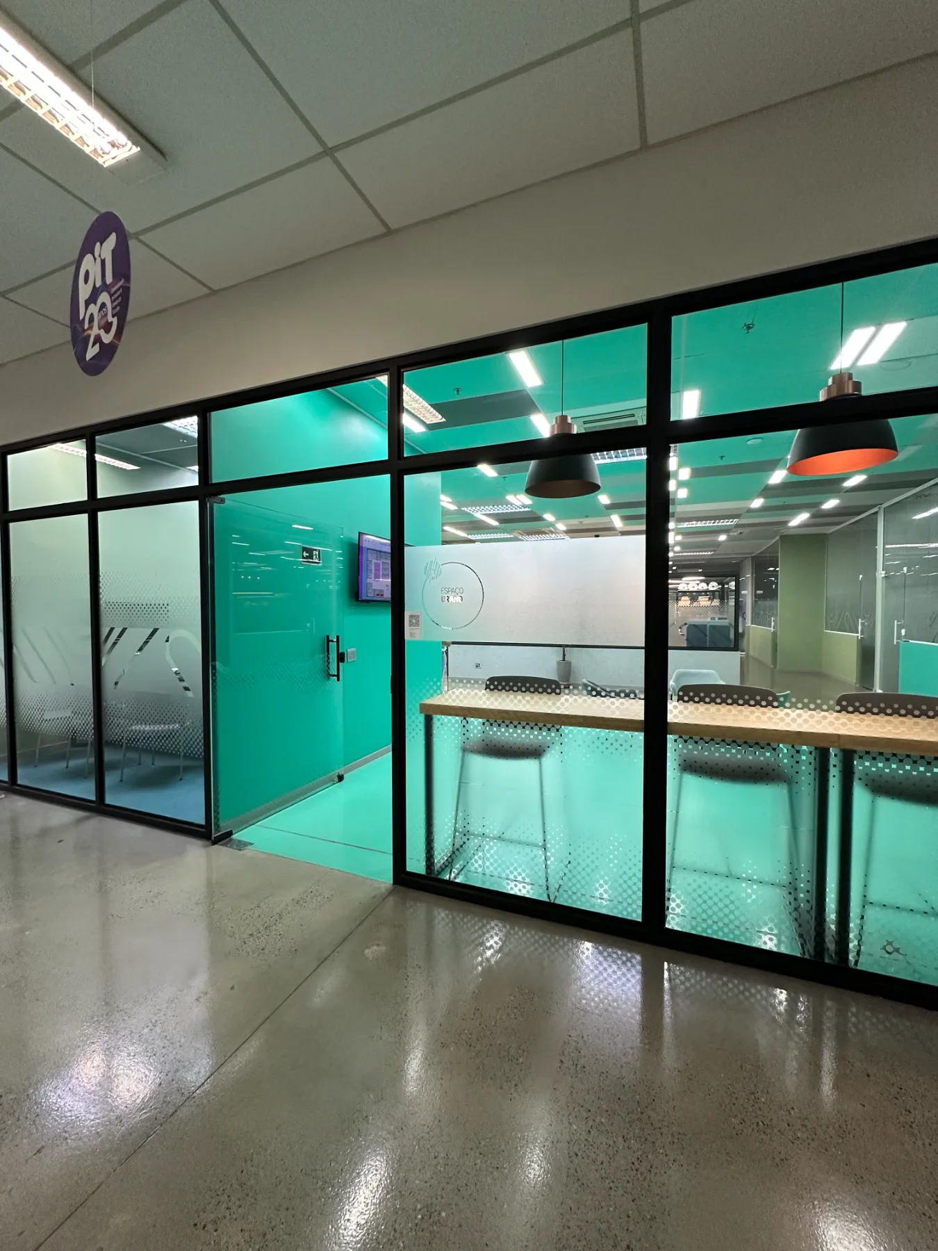 Entrada do Coworking Urano, com marca aplicada no vidro jateado e bancada alta junto à fachada envidraçada