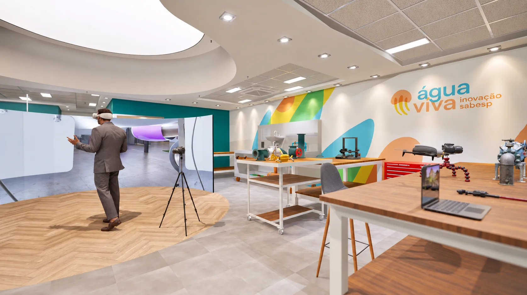 Arena de realidade virtual do Hub: painel curvo de projeção sobre piso de madeira, com usuário de óculos VR, sala de reunião e a marca SABESP ao fundo e bancada expositiva de tubulações à direita