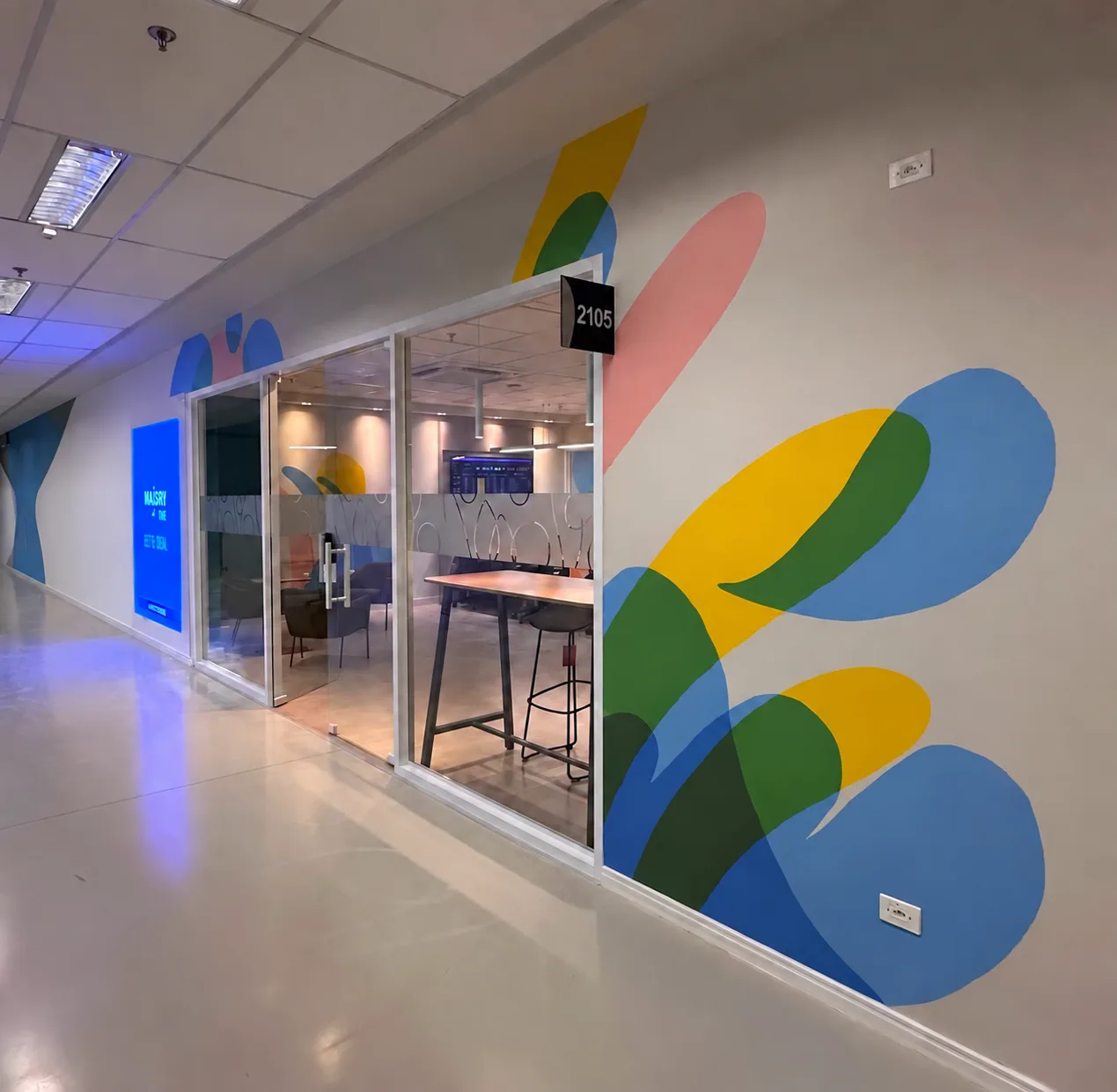 Corredor de acesso ao Hub, com grafismo de parede em cores da identidade e salas de reunião envidraçadas