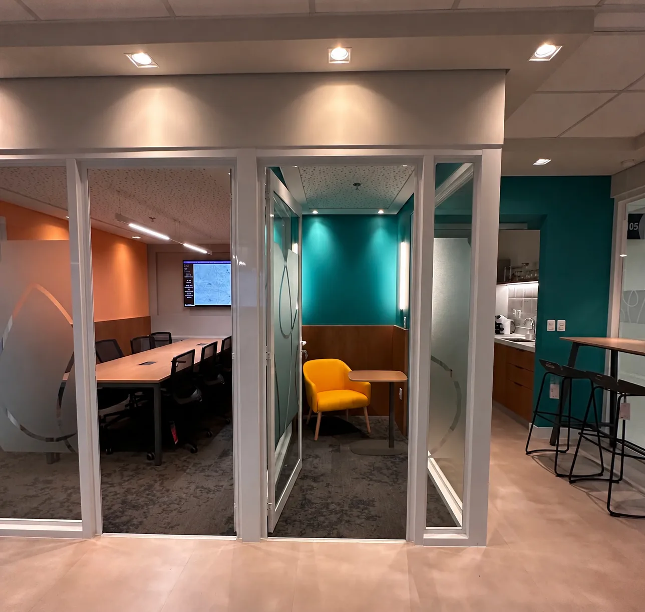 Cabine individual de trabalho em tom turquesa, entre a sala de reunião e a área de apoio