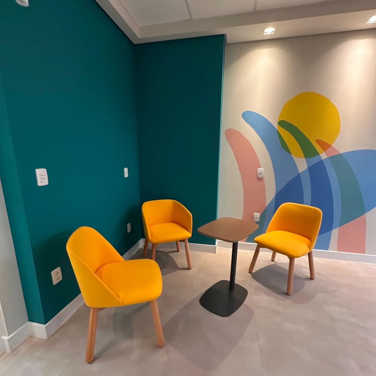 Estar informal com três poltronas amarelas, mesa baixa e painel gráfico na parede