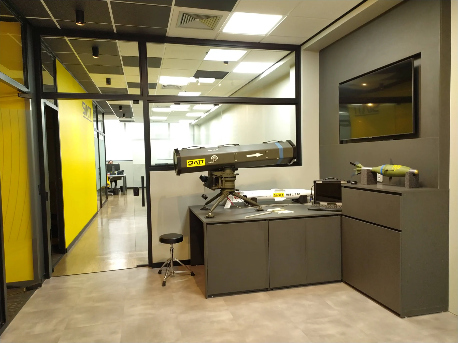 Sala de demonstração com produtos da empresa expostos sobre o balcão, monitor na parede e vedação em vidro voltada para a operação