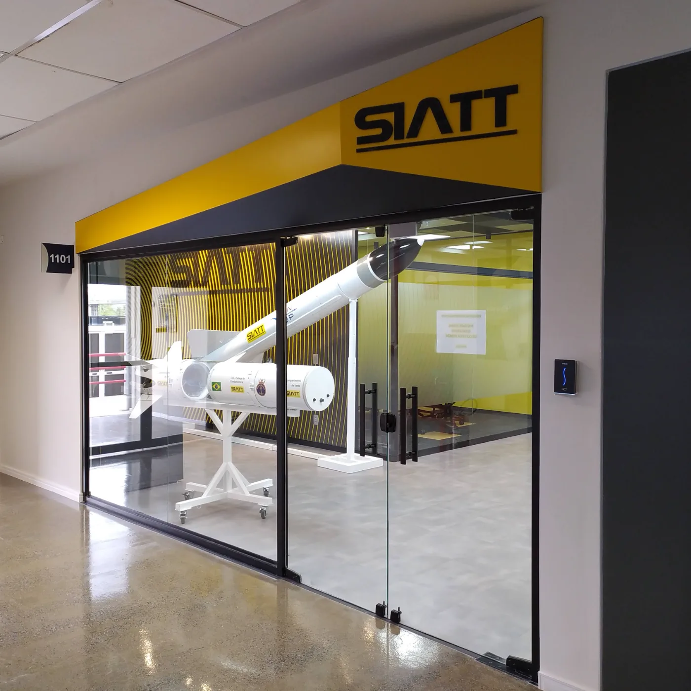 Vitrine executada: fachada envidraçada com a testeira amarela da marca e o míssil em exposição visível a partir da circulação