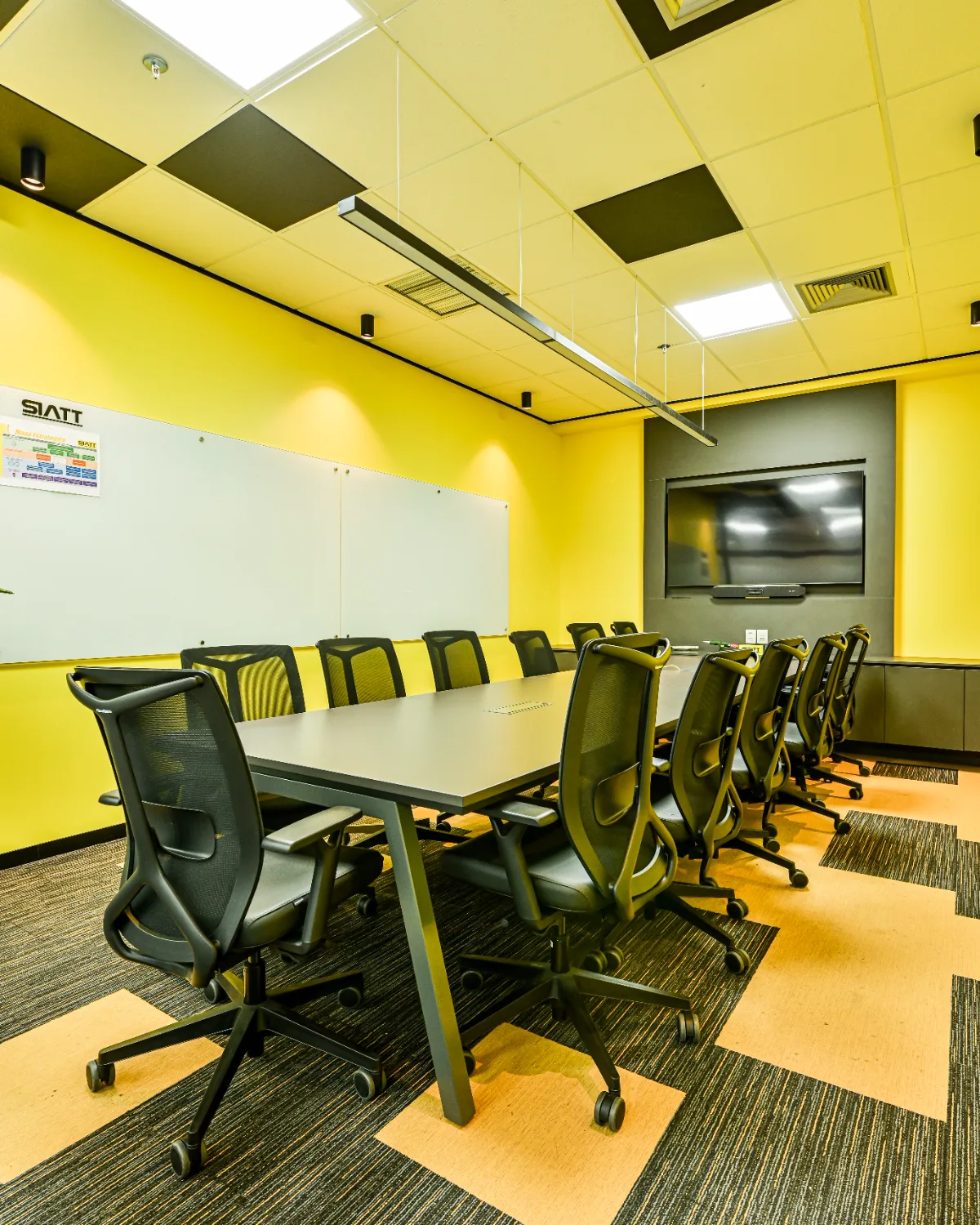 Sala de reunião executada, com mesa longa, cadeiras giratórias, quadro de vidro e monitor sobre painel escuro