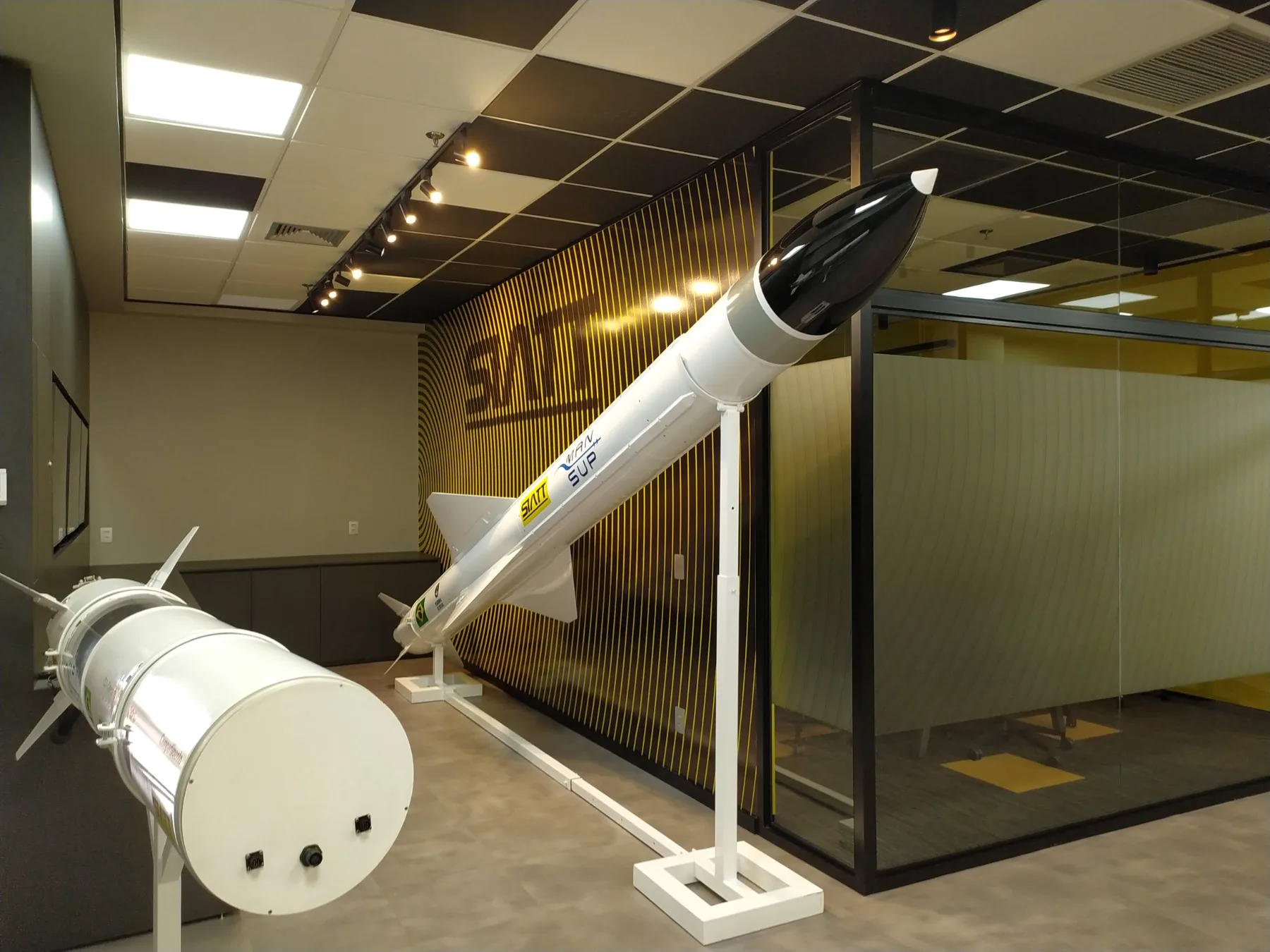Showroom executado, com o míssil MANSUP em suporte branco diante da parede de grafismo amarelo e preto