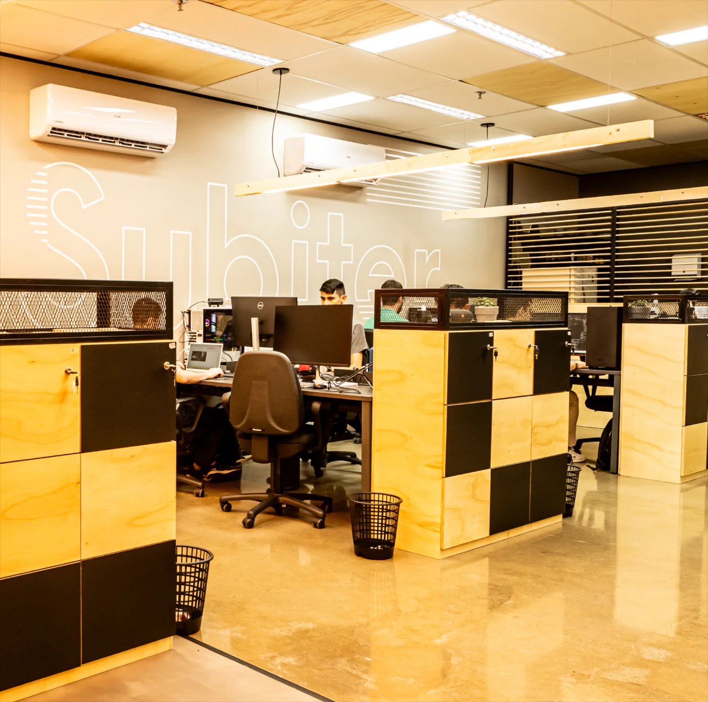Subiter: estações de trabalho em open space com armários de compensado e grafismo da marca na parede