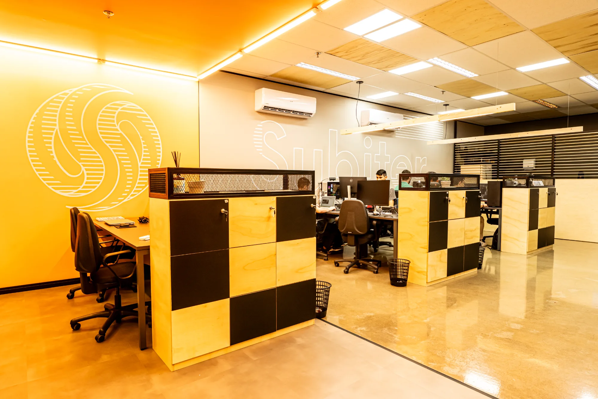 Subiter: estações de trabalho em open space com armários de compensado e grafismo da marca na parede