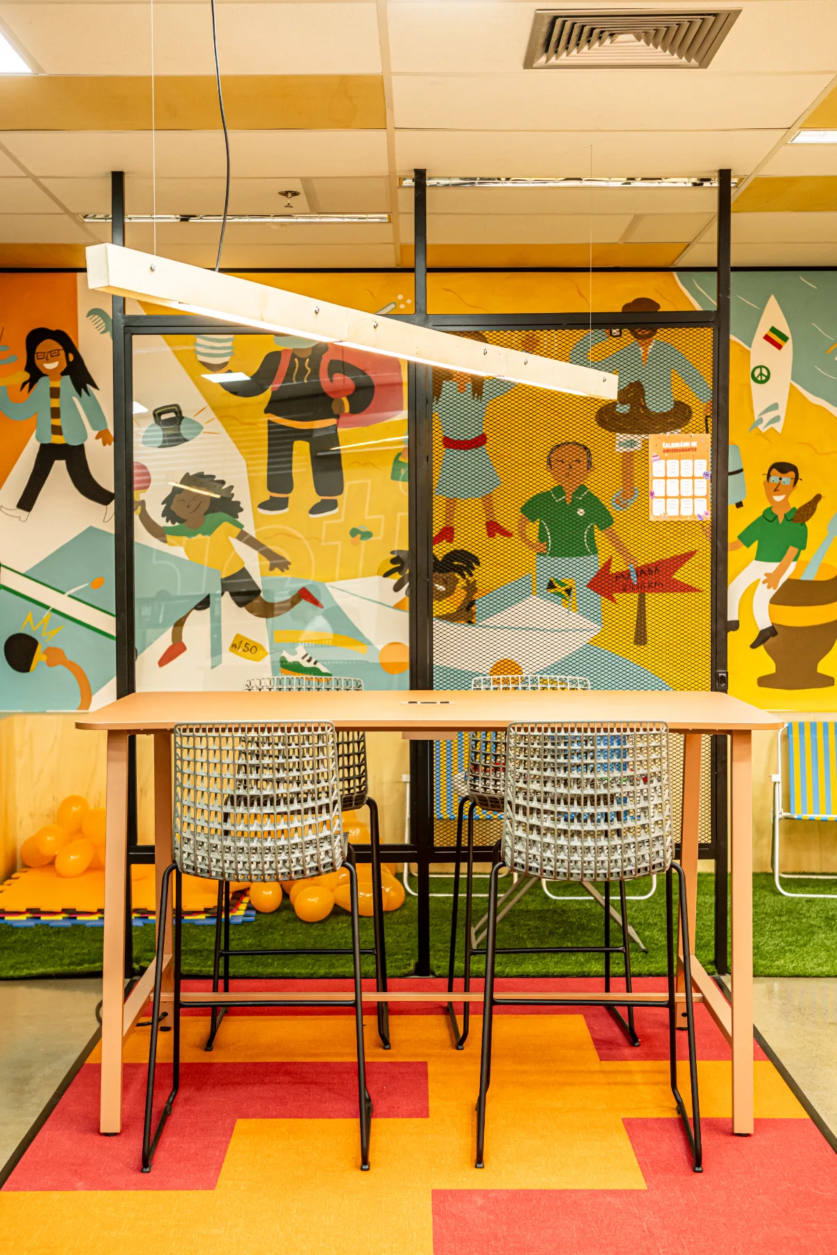 Mural ilustrado com calendário de aniversariantes, luminária linear de madeira e tapete em faixas coloridas